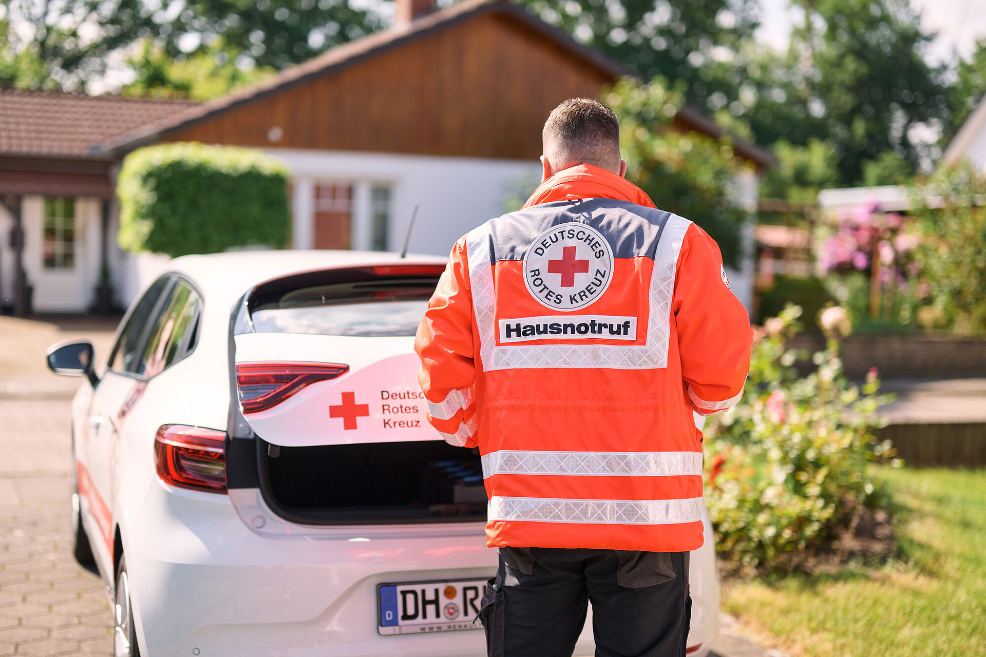 DRK KV Diepholz: Mitarbeiter vom Hausnotruf mit Equipment und Einsatzfahrzeug am Zielort vor dem Haus der Patientin